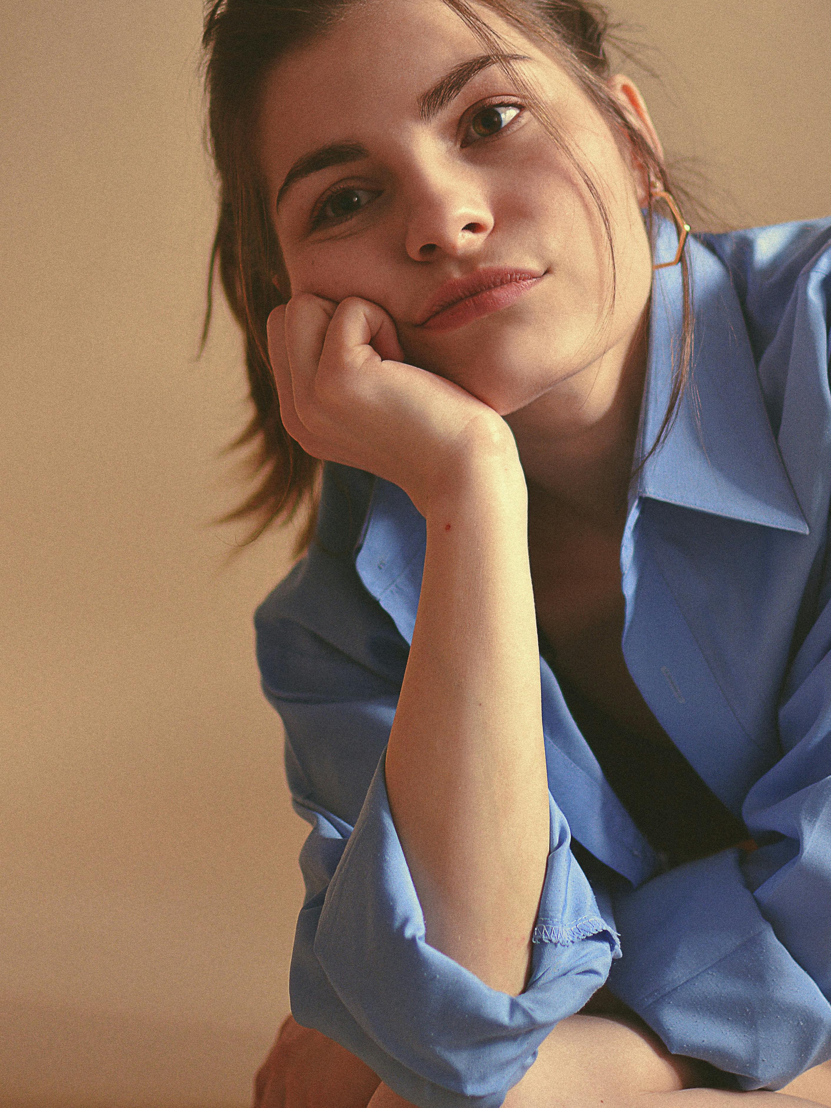 Portrait of a woman in a blue shirt with a contemplative expression, captured indoors.