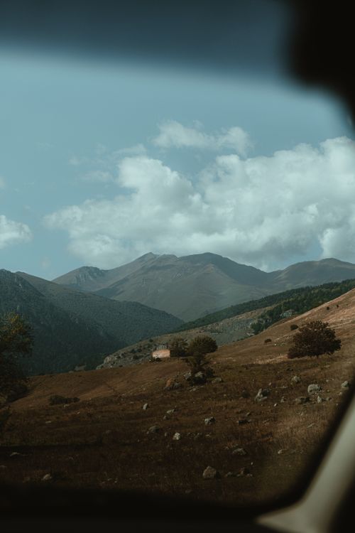 Free Capture the serene beauty of mountains from the comfort of a car with lush trees and clouds. Stock Photo