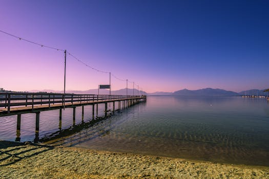 Scenic view of a pier extending into Chiemsee lake with mountains at twilight.