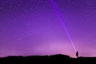 一个人拿着手电筒，站在星光璀璨的夜空下，映衬出空间的美丽