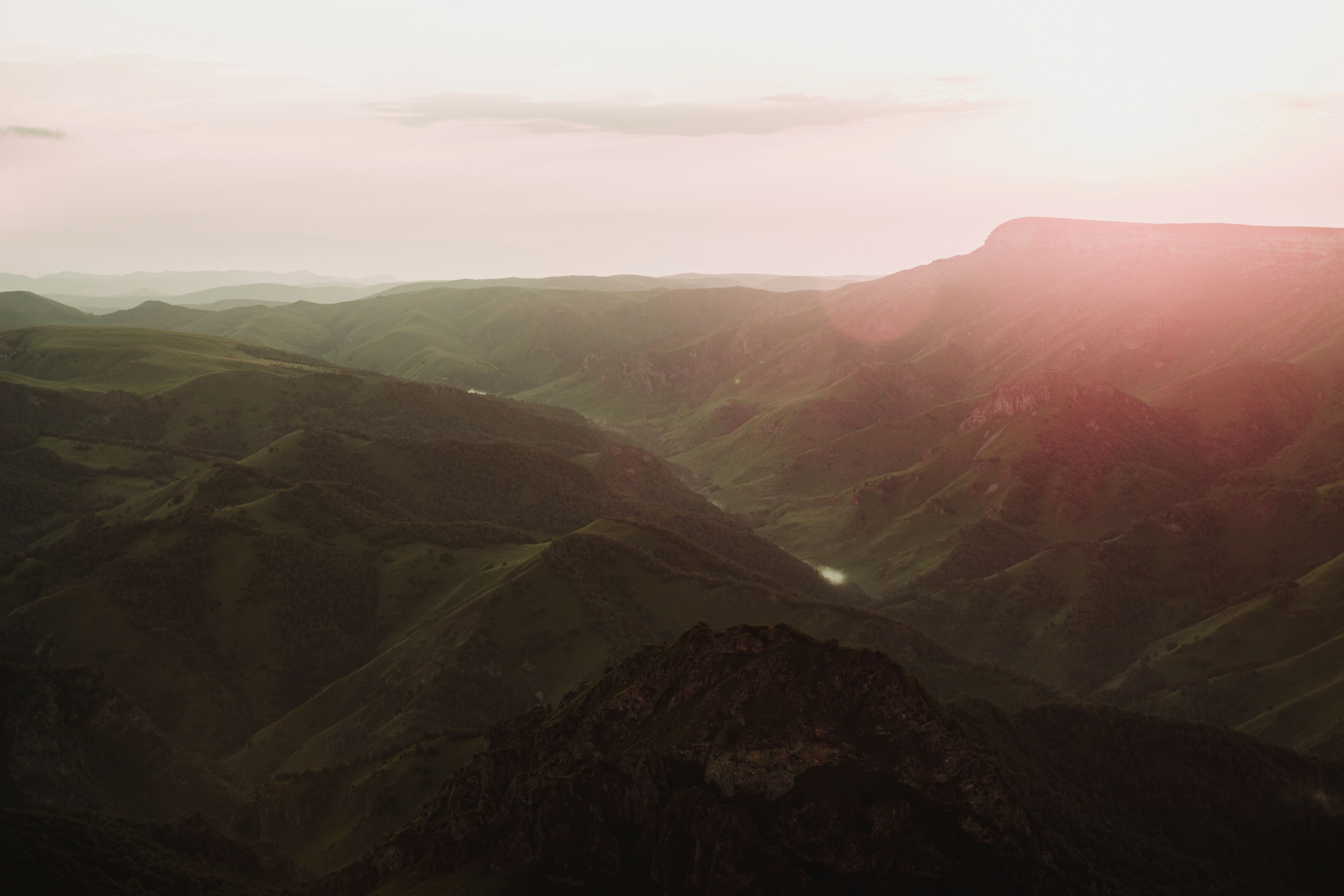 Aerial view of a vast mountain range at sunset, showcasing lush green valleys and sun glare.
