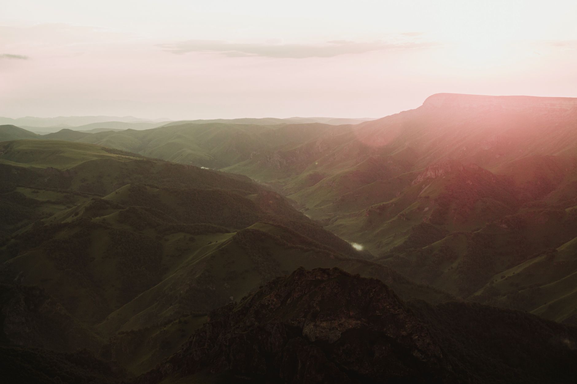 Aerial view of a vast mountain range at sunset, showcasing lush green valleys and sun glare.