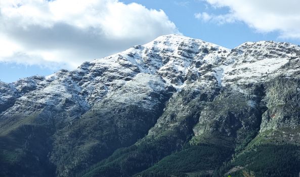 Breathtaking view of snow-capped mountain peaks under a clear blue sky with fluffy clouds.