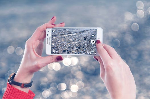 Hands of a woman taking a photograph of pebbles by the water using a smartphone.