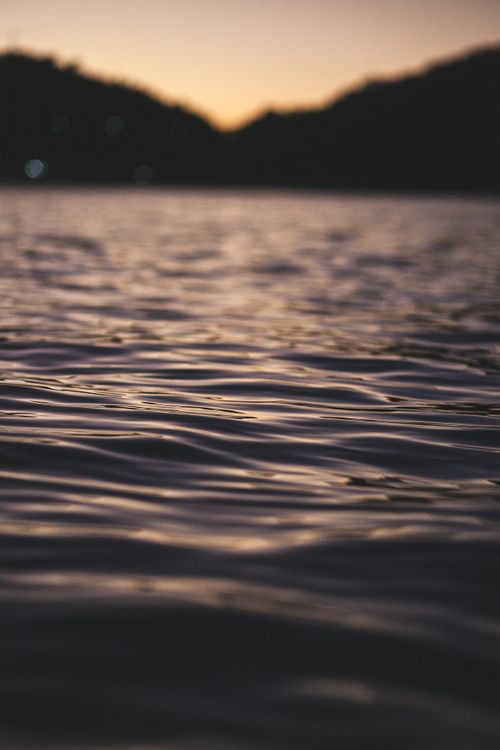 Free Gentle waves on a lake at dusk with silhouetted hills in the background, capturing serene nature. Stock Photo