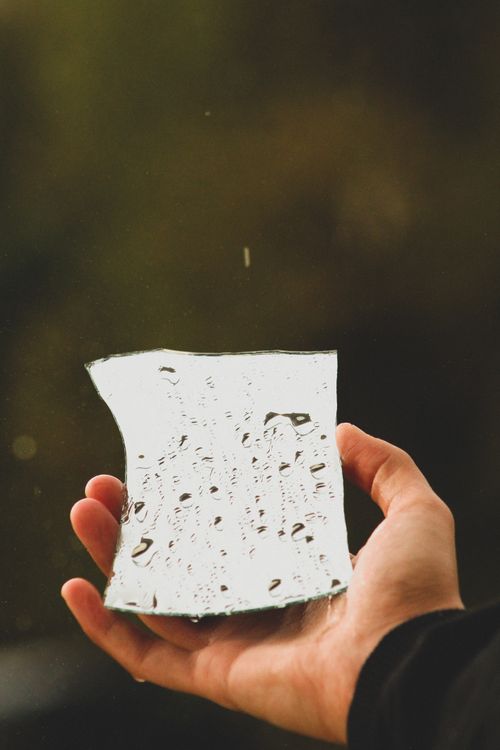 Free Close-up of a hand holding a broken glass mirror with raindrops on a blurred outdoor background. Stock Photo
