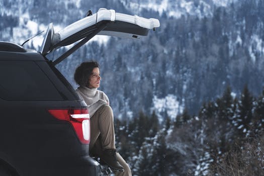 Woman sitting in SUV trunk enjoying a peaceful winter mountain view.