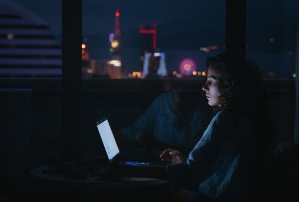 Attendee working late on a laptop above a lit skyline — Beka Ichkiti on Pexels