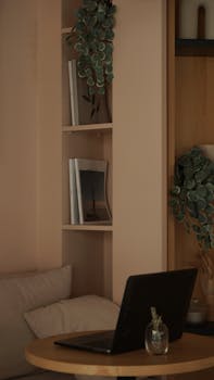 Stylish indoor setup featuring a laptop on a table, bookshelves, and greenery.