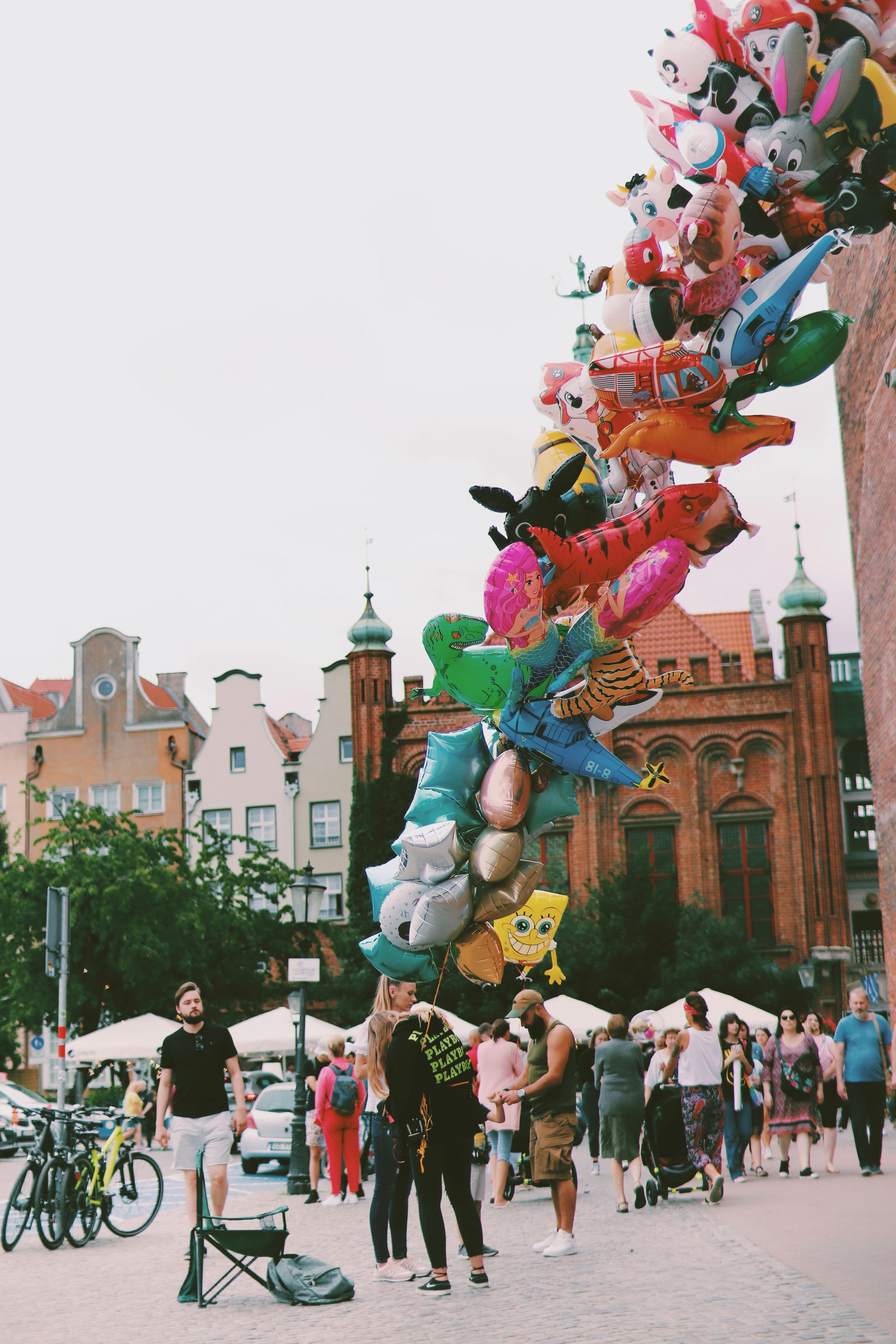 Vibrant assortment of balloons in a lively urban setting with people strolling around.