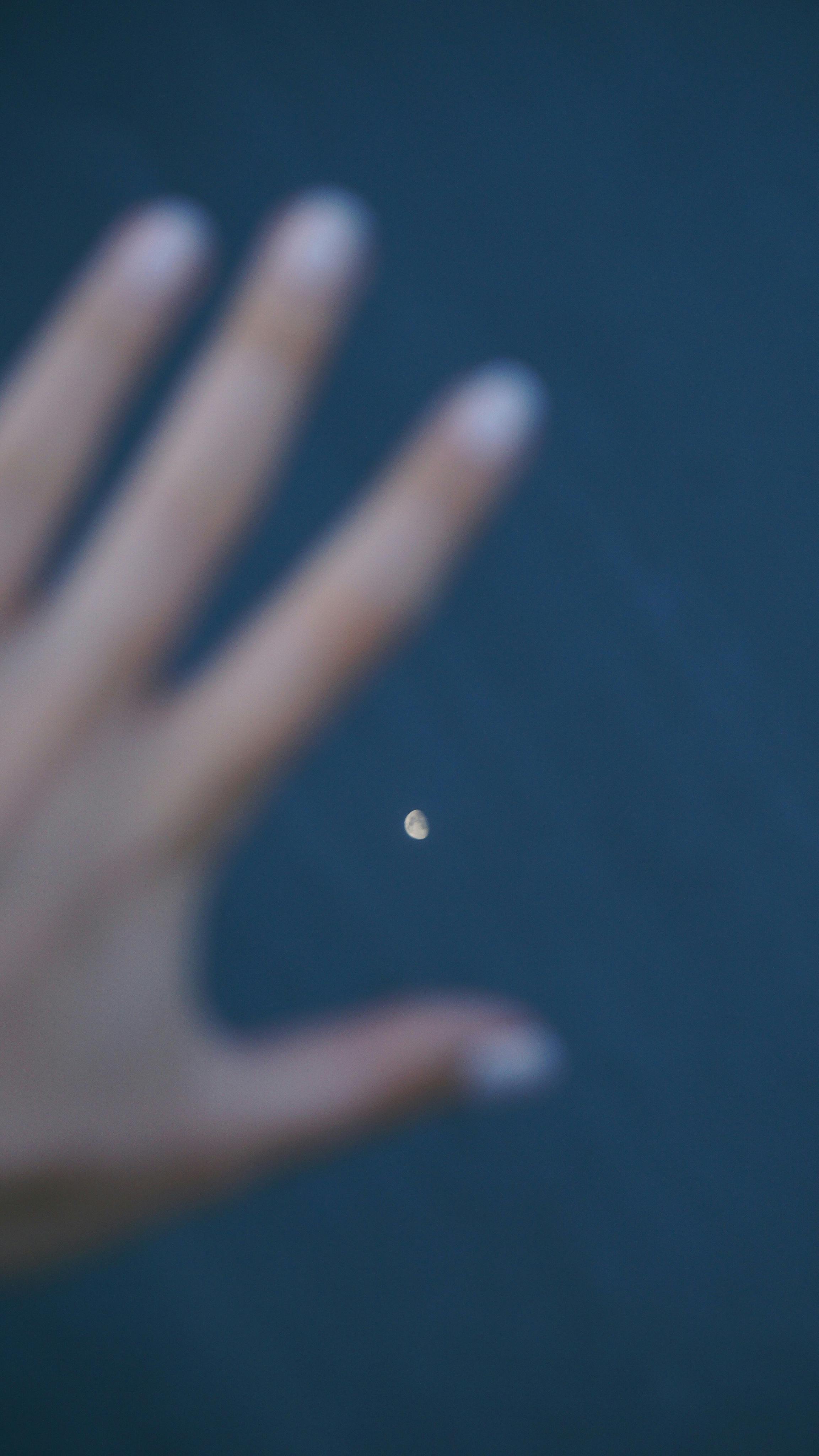 A soft focus image of a hand reaching towards the moon in a dark sky.