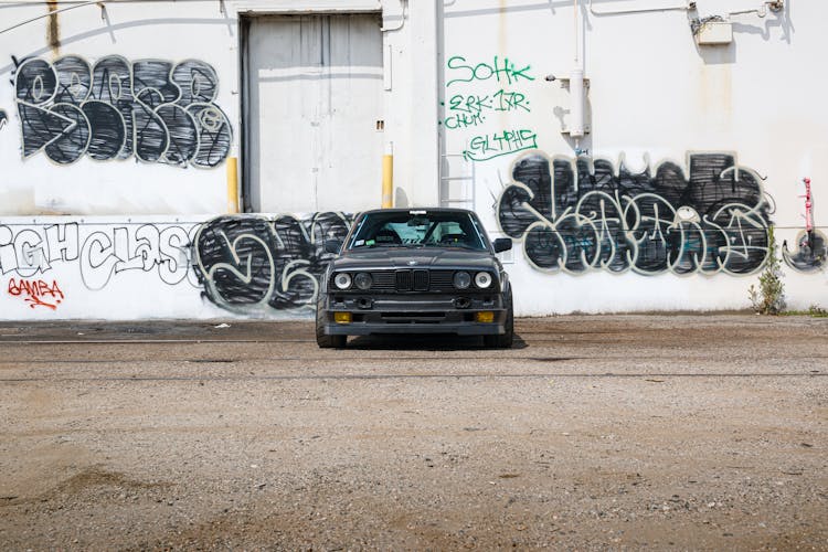 A Black Car Parked Near The Wall With Vandalism