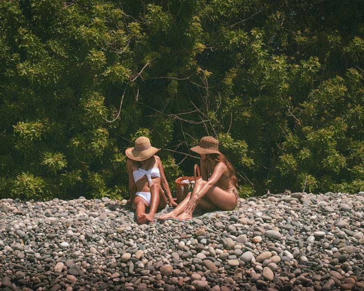 Women Straw Hats Sunbathing On A Rocky Beach 