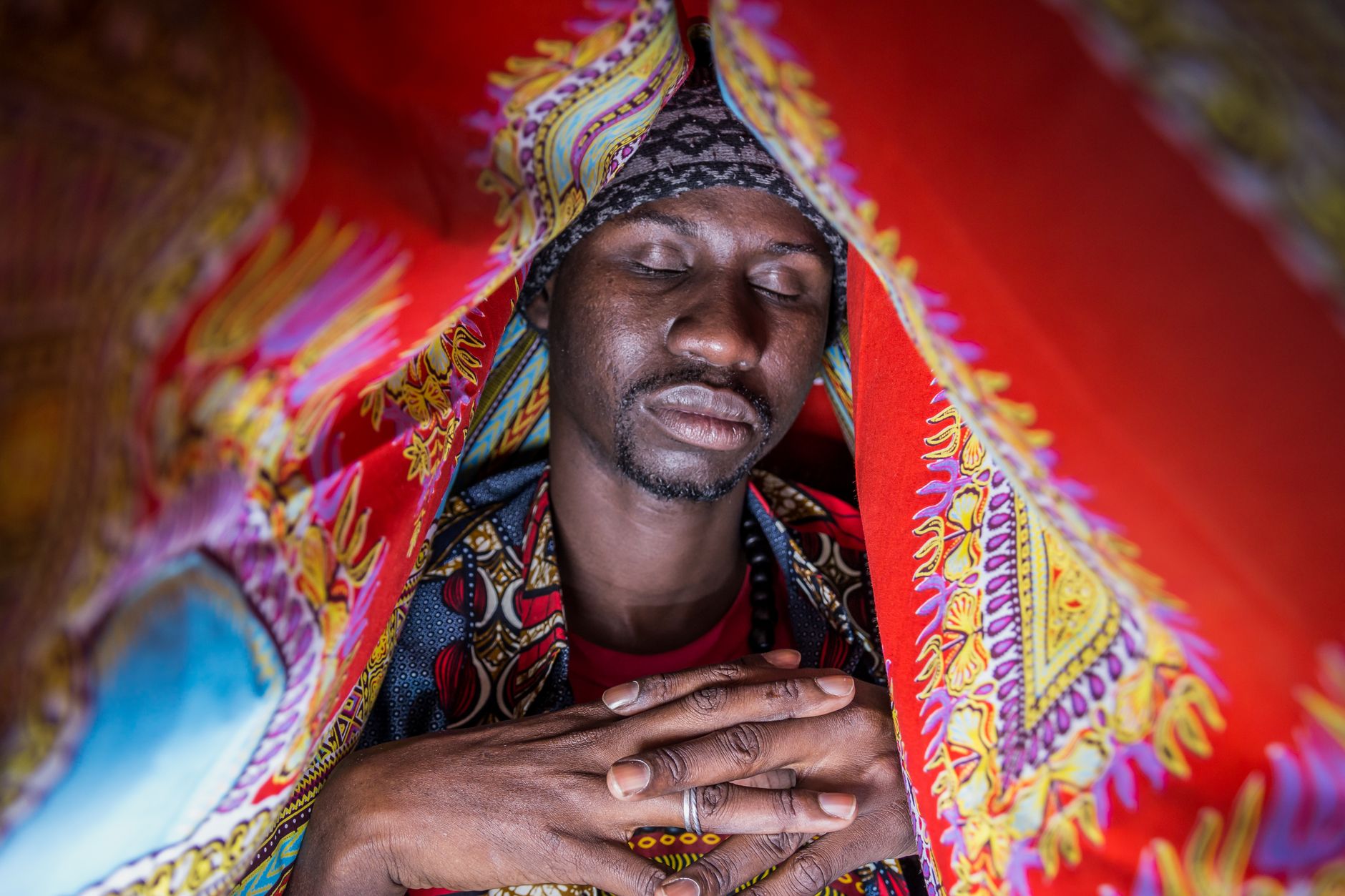 A contemplative African man meditates under colorful textiles, creating a serene ambiance.