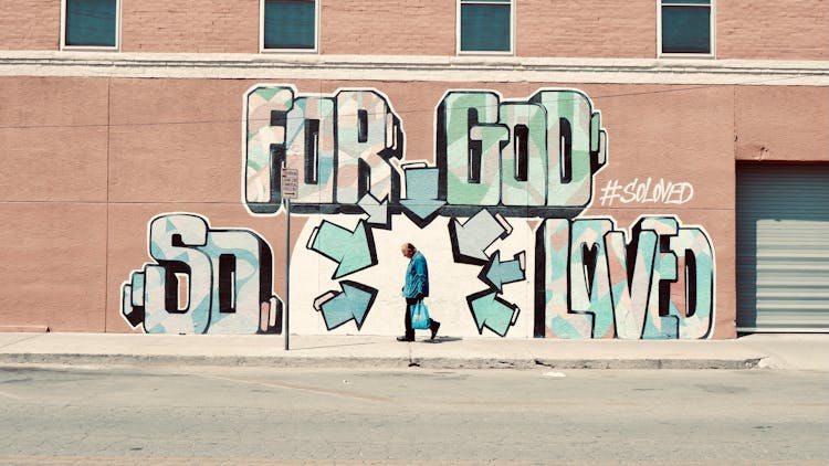 A Man Walking On The Street Near The Graffiti Wall