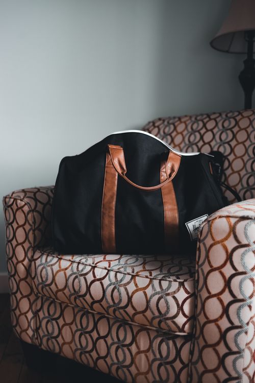 Free A chic black duffel bag with brown accents sits on a stylish patterned armchair indoors. Stock Photo