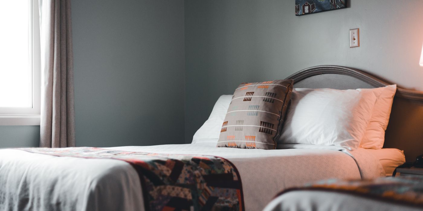 A neatly arranged hotel room bed beside a bright window