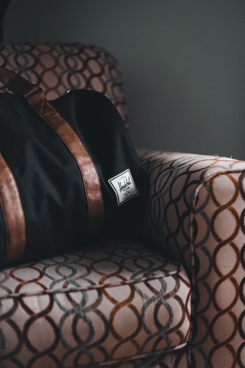 Free Close-up of a duffle bag with leather straps on a patterned armchair, showcasing stylish and modern design. Stock Photo
