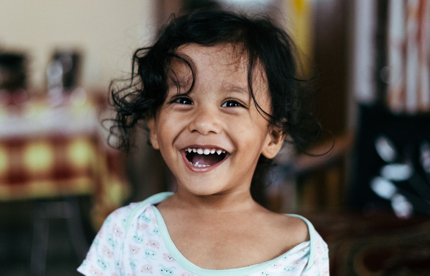 Adorable child with curly hair joyfully laughing indoors, capturing pure happiness.