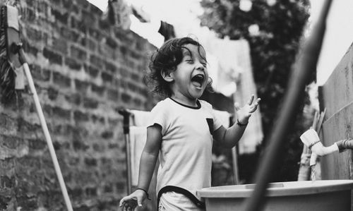 Free Black and white photo of a happy toddler playing near a water faucet outdoors. Stock Photo