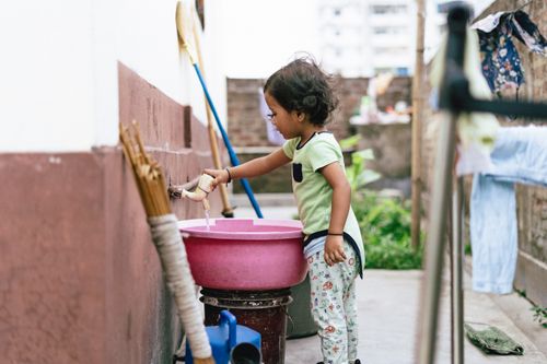Free A young child in a casual setting fills a pink basin with water outside, showcasing daily life. Stock Photo