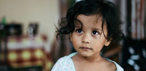 Free Portrait of a young girl with curly hair, looking thoughtful indoors. Stock Photo