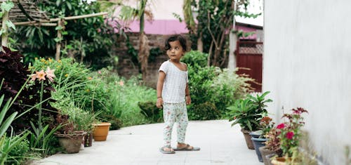 A Kid Standing on the Backyard Between Potted Plants
