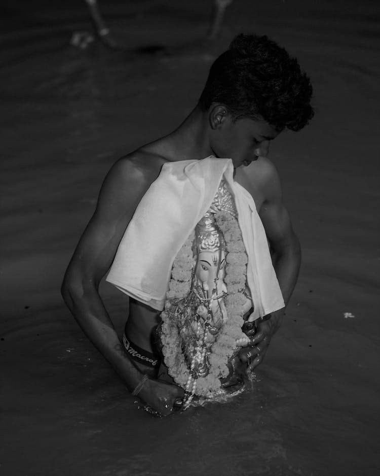 Grayscale Photo Of A Young Man Holding A Figurine While Standing On The Water