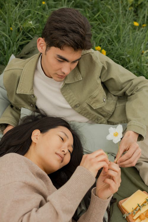 Free A young couple enjoys a peaceful moment lying on grass, holding a flower. Stock Photo