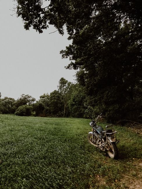 A classic vintage motorbike parked in a lush green field under a cloudy sky.