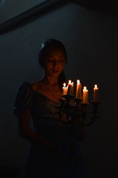 A woman holding a candelabra in a dimly lit room, creating a moody ambiance.