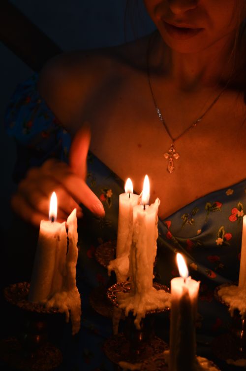 Free A woman in a dimly lit room surrounded by burning candles with flowing wax, creating a serene ambiance. Stock Photo