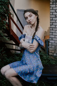 Young woman sitting outdoors in a floral dress, embracing a book, exuding calmness.