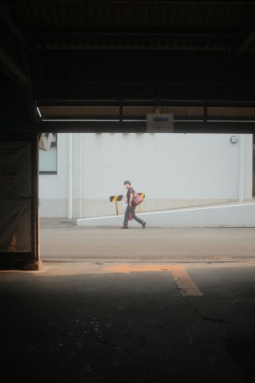 Free A person is walking outdoors, visible through an industrial structure, casting a soft shadow. Stock Photo