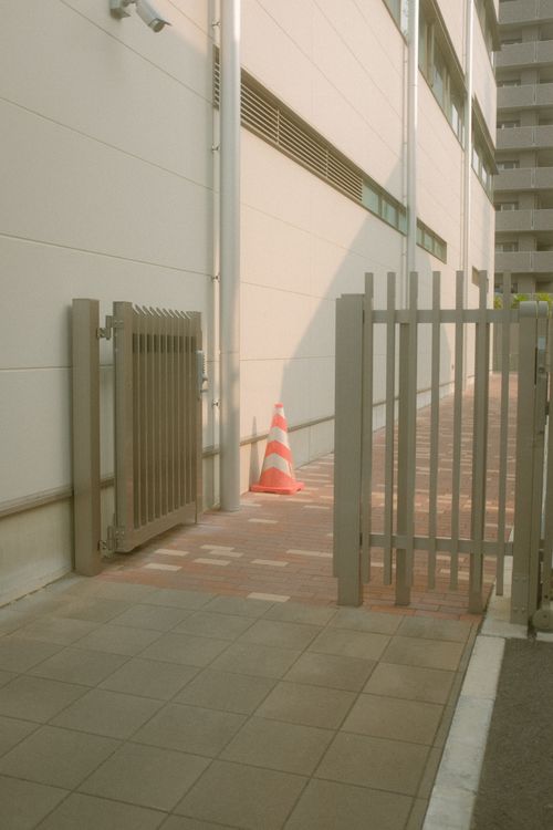 Free A city entrance featuring a modern gate and traffic cone on a sunlit sidewalk. Stock Photo