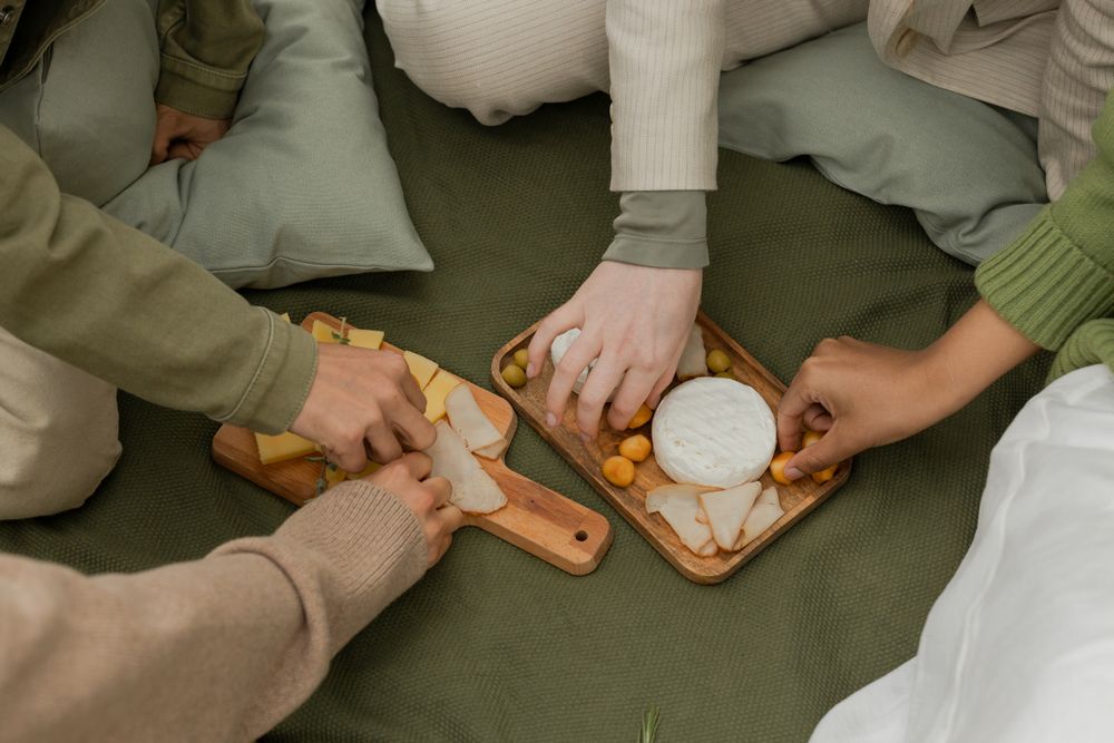 Four members reaching across a shared board of farmhouse wheels on a picnic blanket, photo by Ron Lach
