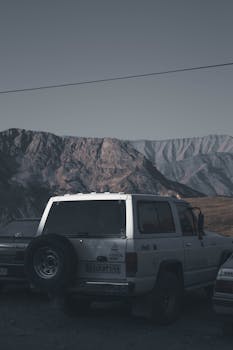 Parked off-road vehicles with rugged mountainous backdrop in Iran's desert at dawn.