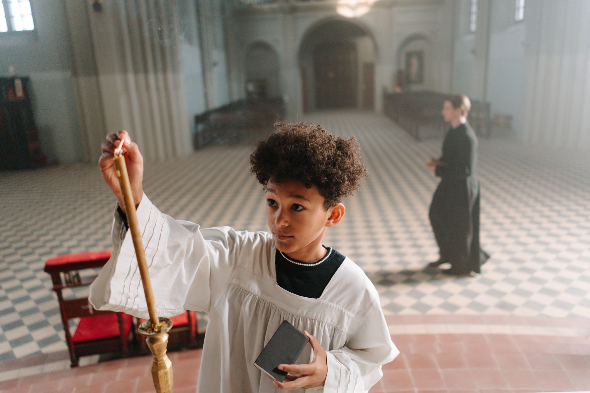 Child acolyte lighting candle inside a cathedral during a religious ceremony.