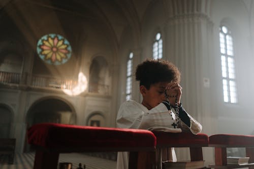 A Boy Praying and Kneeling Inside a Church