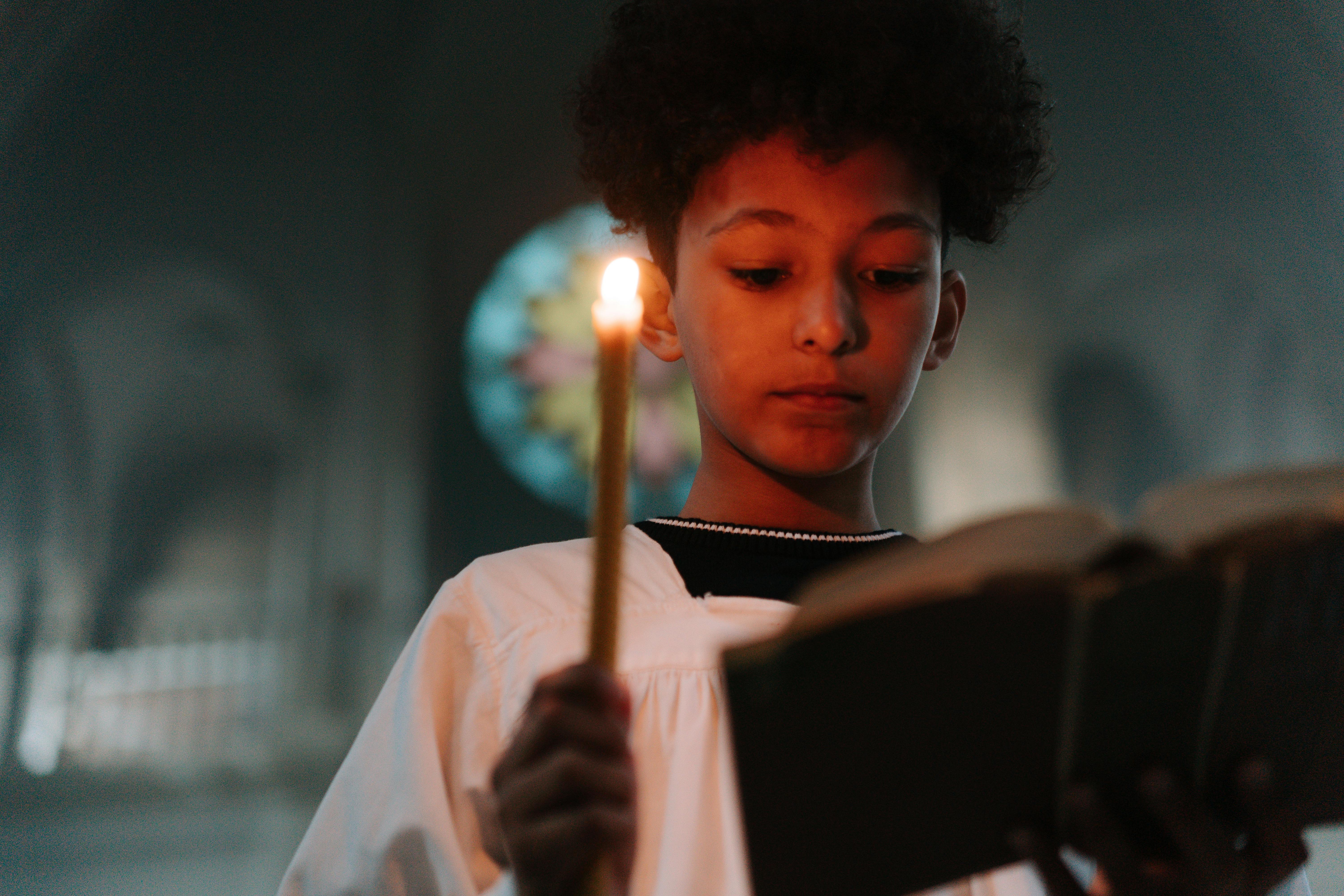 young boy reading book while holding a candle