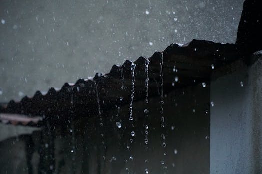 Close-up of rainwater flowing off a corrugated roof in low light, creating a serene ambiance.