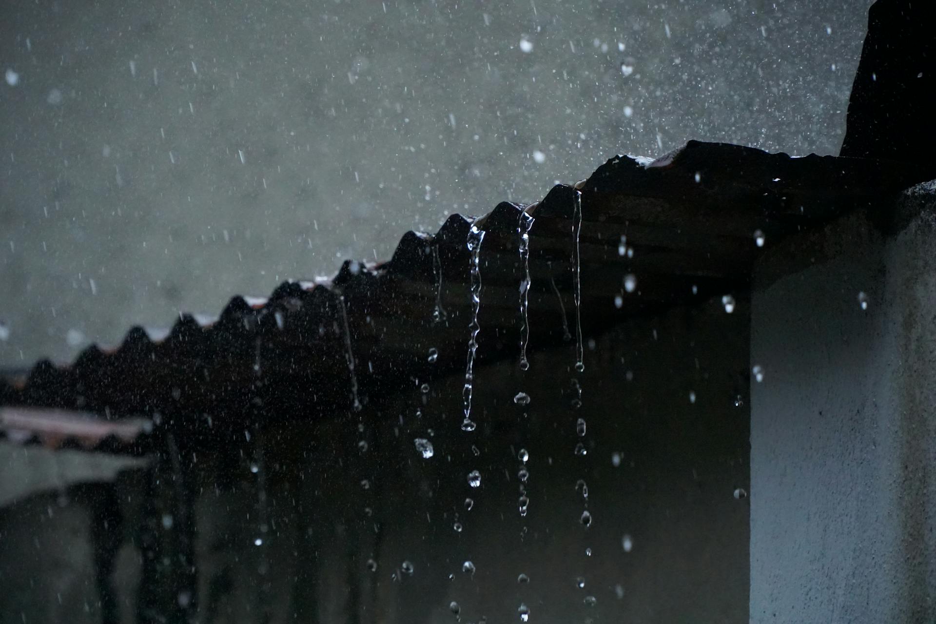 Close-up of rainwater flowing off a corrugated roof in low light, creating a serene ambiance.