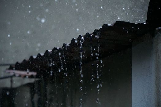 Close-up of rainwater cascading from a corrugated roof in Long Khánh, Vietnam.