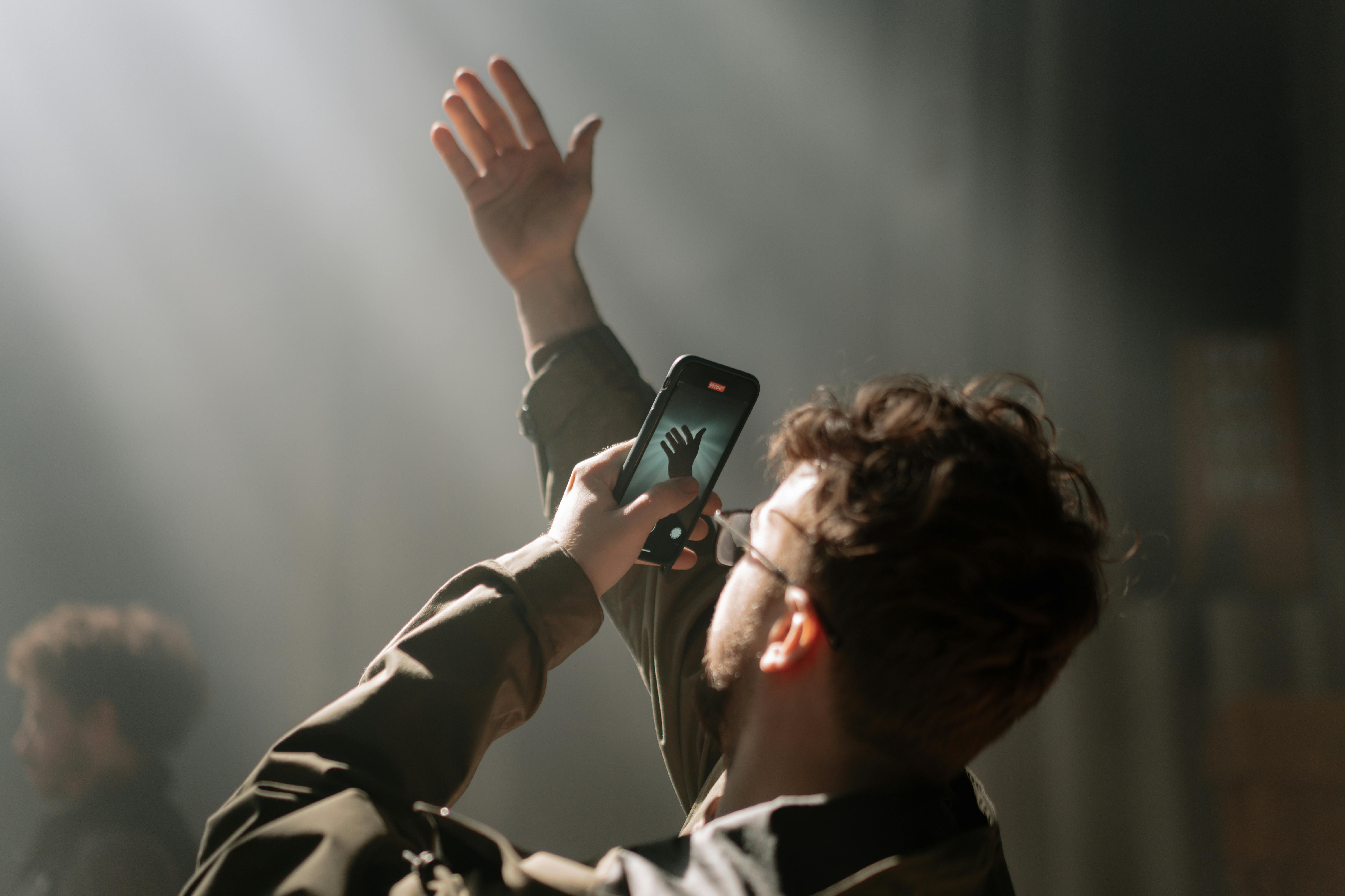 Free Adult male using smartphone for capturing photo in dramatic indoor lighting. Stock Photo