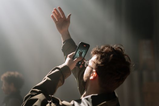 Adult male using smartphone for capturing photo in dramatic indoor lighting.