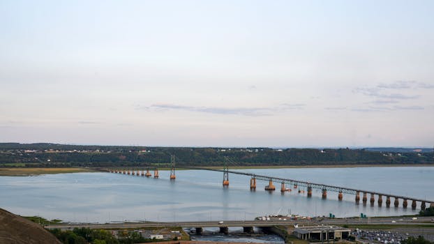 Expansive view of a long industrial bridge crossing a wide river, with surrounding greenery.