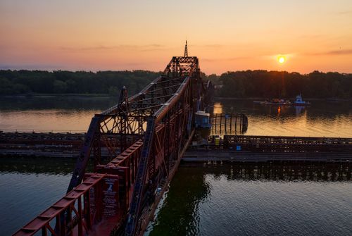 Free Picturesque sunset over a swing bridge crossing a river, showcasing vibrant colors and serene water reflections. Stock Photo