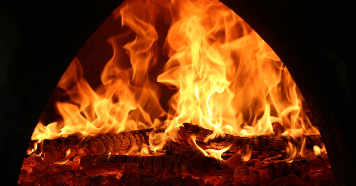 Intense flames consuming wood in a dark oven setting, creating warmth.