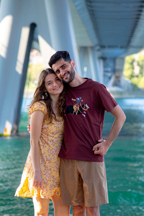 Man in Maroon Crew Neck T-shirt Standing Beside Woman in Yellow Floral Dress