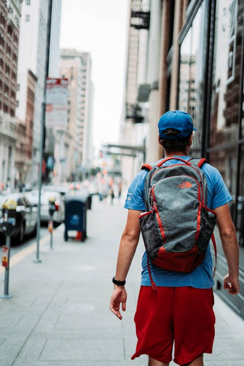 Backview of Man in Blue and Red Backpack Walking on Sidewalk